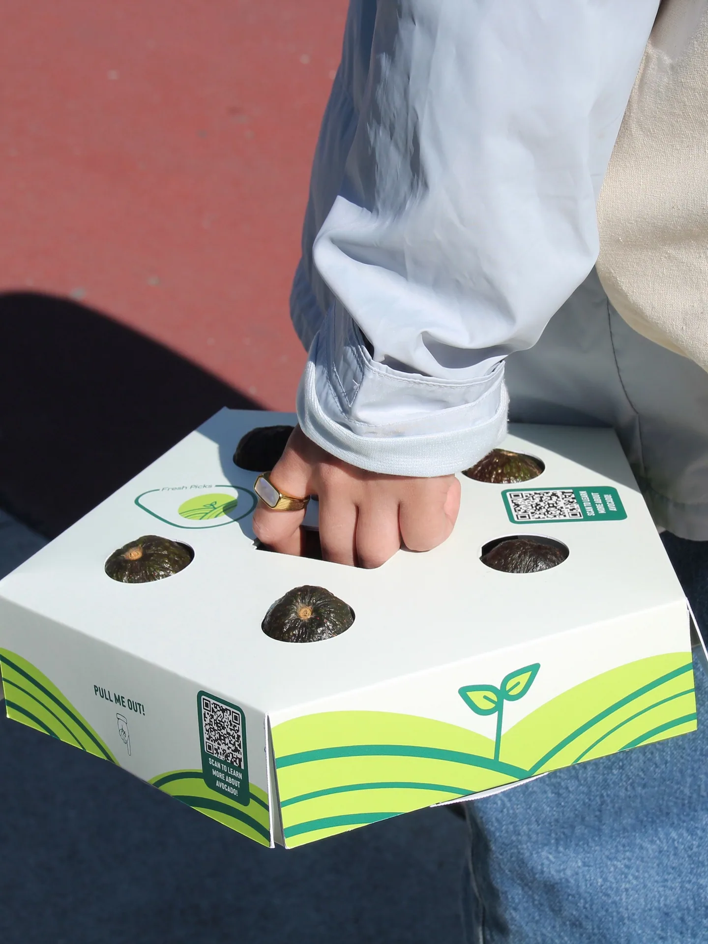 A hand carrying the Fresh Picks pentagonal avocado carrier by its handle