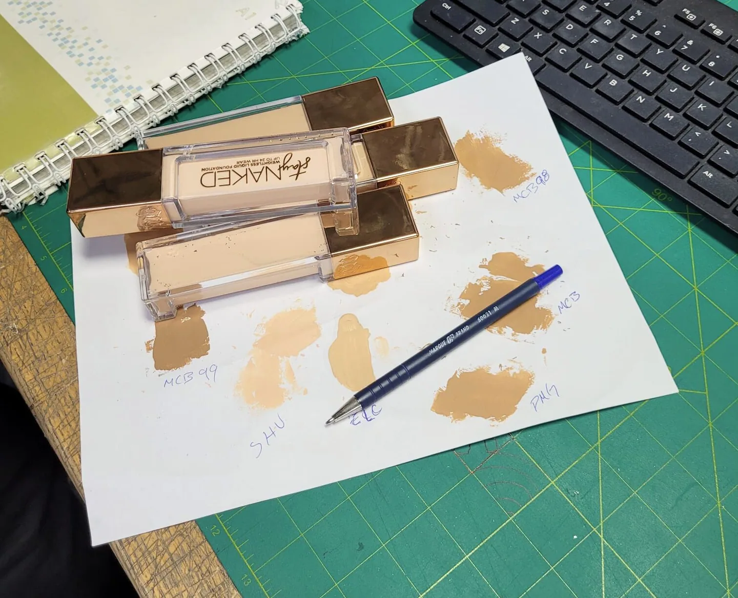 Foundation swatches on paper beside sample bottles on a cutting mat